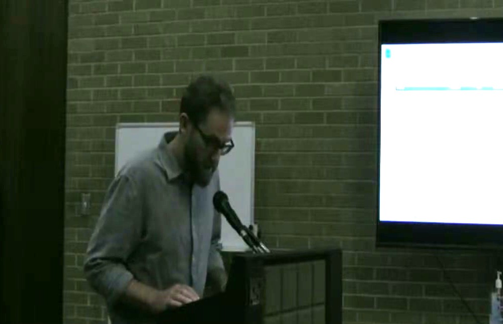 Robert Cheek at the council podium on September 24, 2024, with the water-rate presentation on the screen behind him